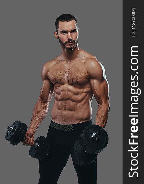 A Muscular Guy Working Out With Dumbbells. Isolated On A Gray Ba