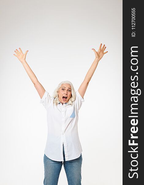 Beautiful female pensioner 60s with gray hair raising her arms and screaming like happy woman isolated over white background