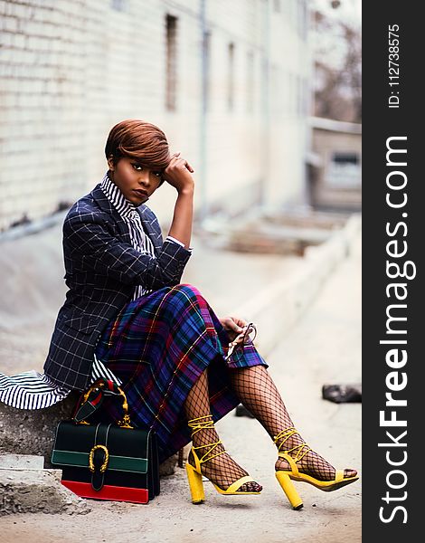 Woman Wearing Black And Grey Tattersall Blazer And Multicolored Plaid Skirt With Black Mesh Stocking And Yellow Chunky Heeled Sand