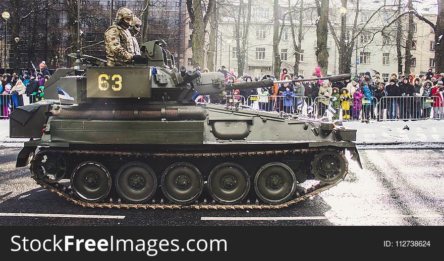 Two Soldiers Ride on Green Military Tank Surrounded With People