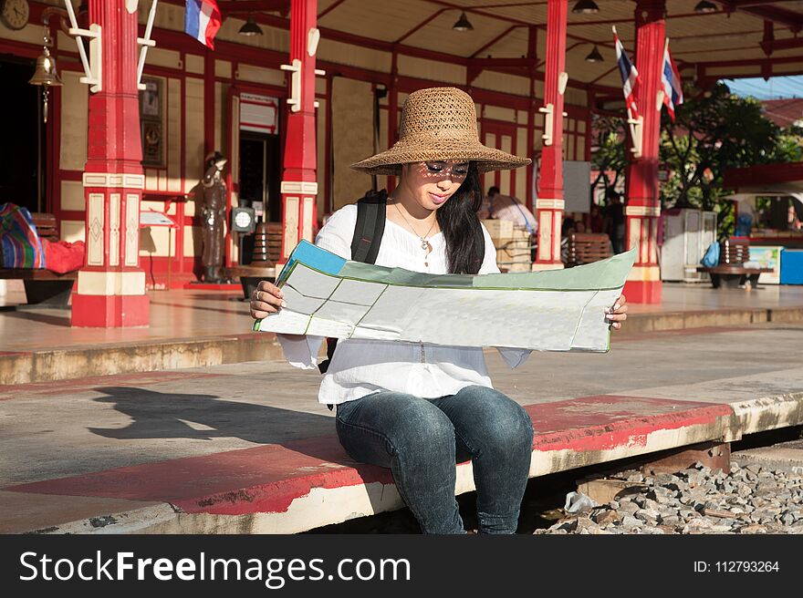 Pretty Asian traveler backpacker female looking map at railway station in Thailand.