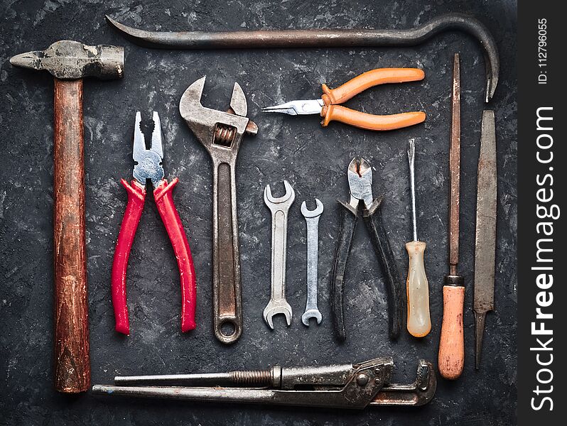 Many Working Tools On A Black Concrete Table. Nippers, File, Pliers, Scrap, Hammer, Wrench, Screwdriver. Top View. Flat Lay