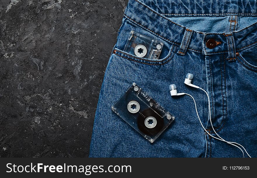 Jeans, audio cassette, headphones layout on a black concrete table. Conceptual photo
