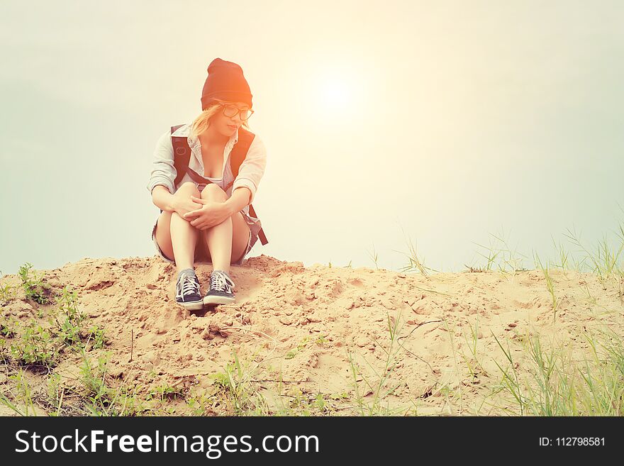 Young hipster woman sitting on the sand and carrying backpack feeling so sad