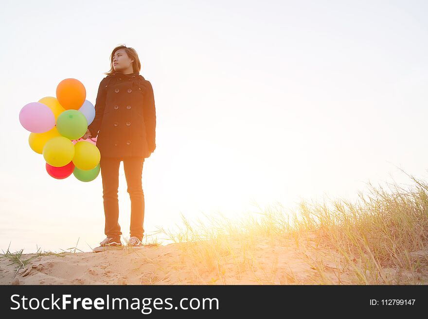 Beautiful young woman holding balloons wearing black coat in the winter feeling sadly