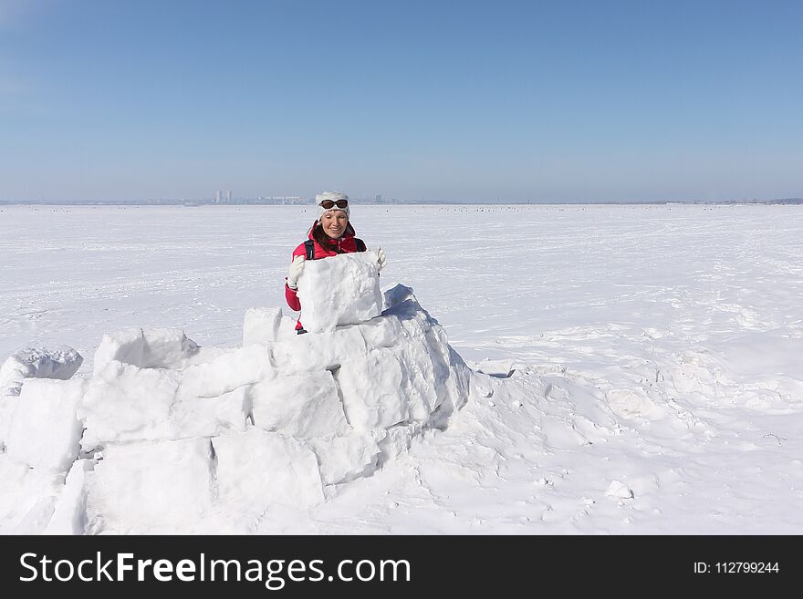Happy woman a red jacket building an igloo on a snow glade in the winter, Siberia, Russia