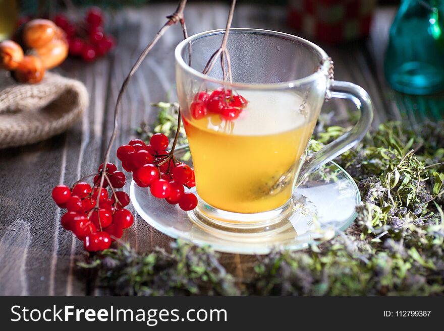 Herbal tea from the viburnum decoction of red sea buckthorn berries and thyme in a transparent glass mug in the village on a wooden table. Herbal tea from the viburnum decoction of red sea buckthorn berries and thyme in a transparent glass mug in the village on a wooden table