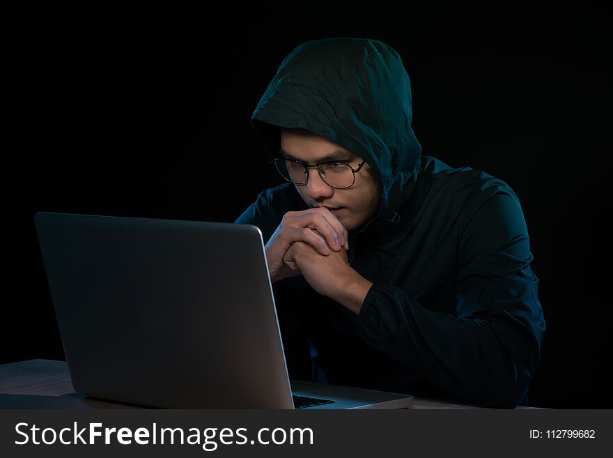 Hacker in a dark hoody sitting in front of a notebook. Computer privacy attack