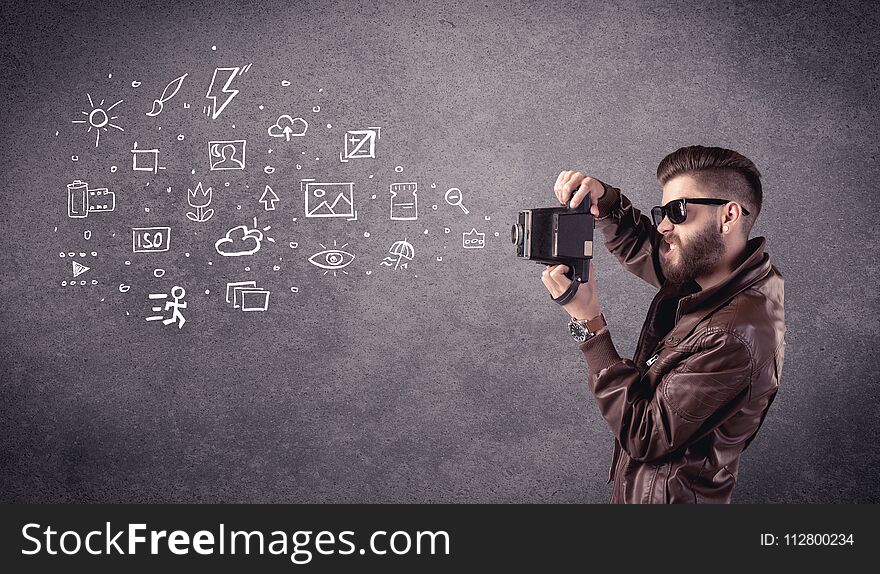 An elegant hipster guy trying to use a vintage camera with camera settings icons drawn on wall, like flash, white balace or ISO value concept. An elegant hipster guy trying to use a vintage camera with camera settings icons drawn on wall, like flash, white balace or ISO value concept