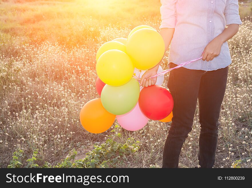 Hipster woman`s hands holding multi color of balloons in the meadows