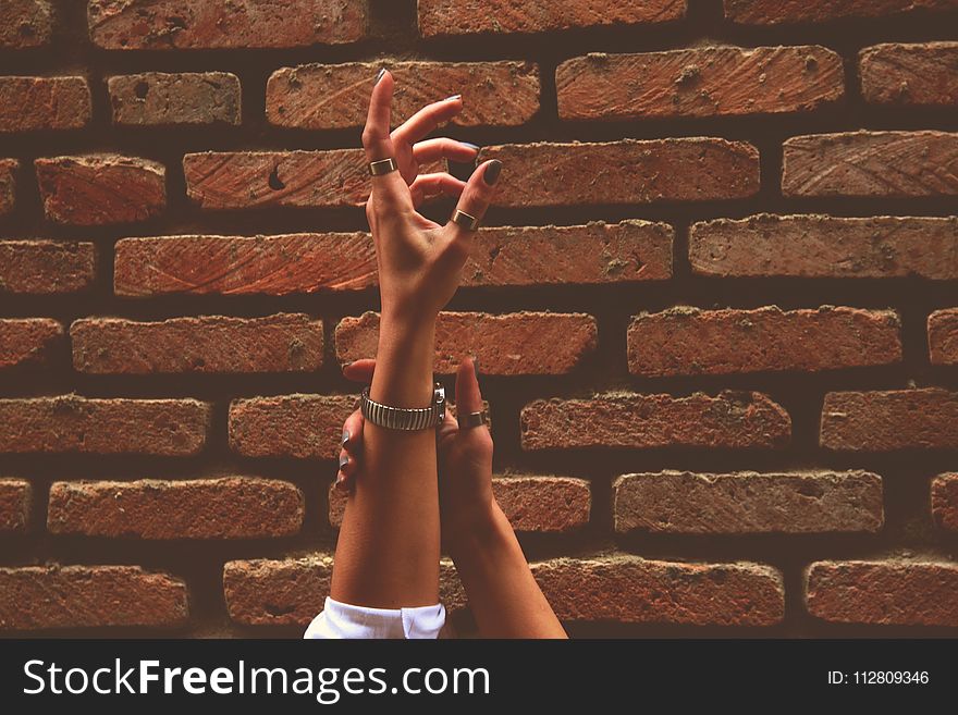 Person Wearing Watch and Rings Raising Left Hand Near Brick Wall