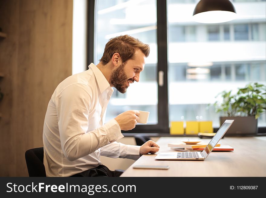 Man Holding Teacup Infront of Laptop on Top of Table Inside the Room