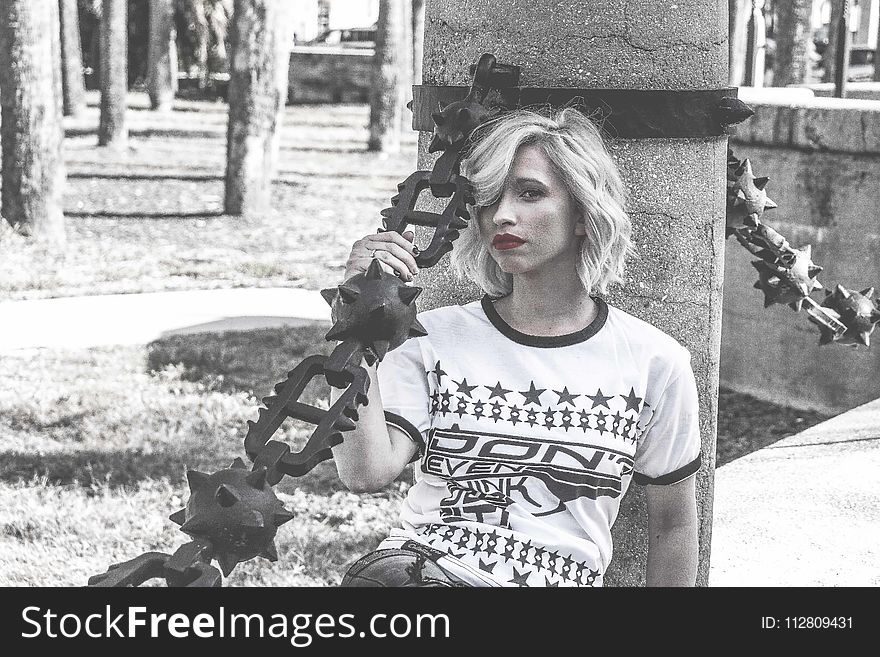 Selective Color Photography Of Woman Laying Her Back At Concrete Column Holding Spike Chain