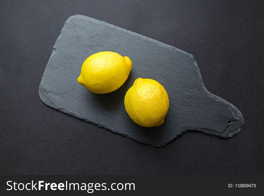 Two Lemons on Black Wooden Pad
