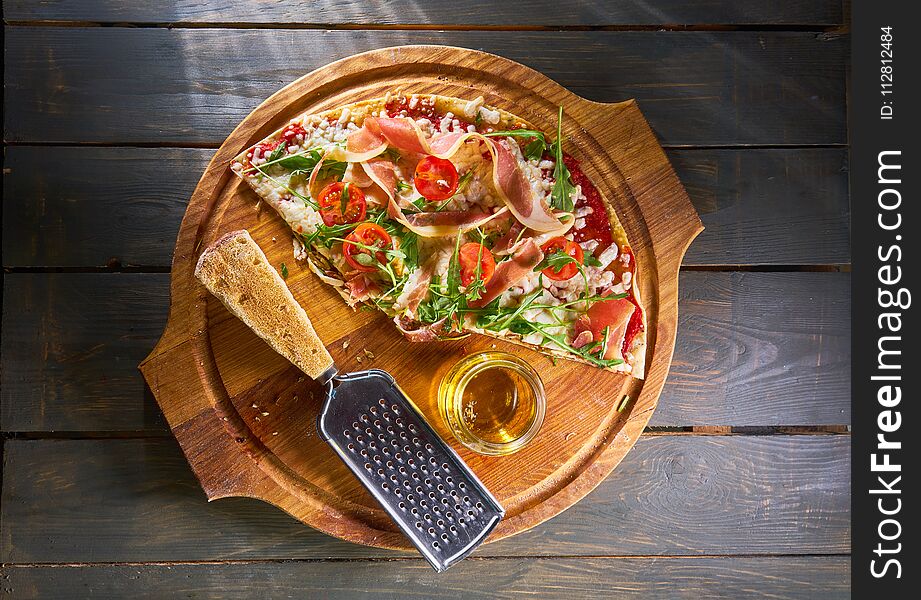 Italian pizza with ham, tomatoes, cheese and herbs on vintage wooden background.