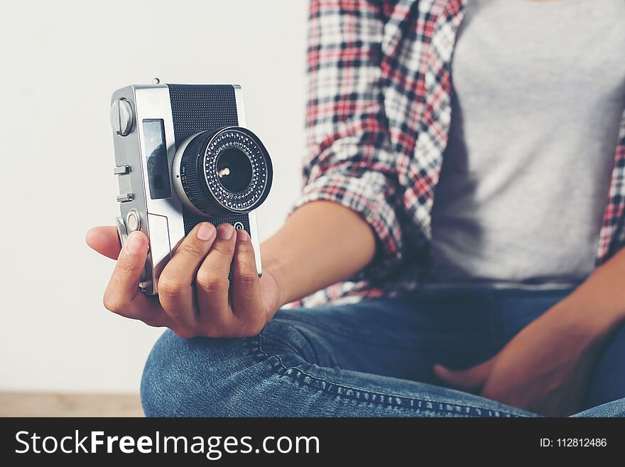 Young hipster photographer hand holding retro camera sitting on wooden floor background