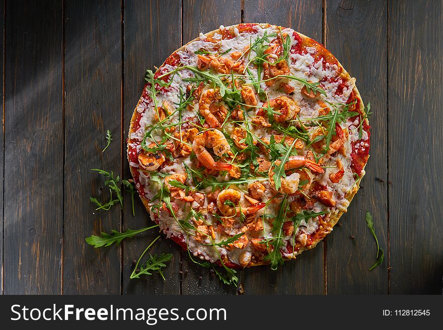 Tasty pizza with shrimp, mozzarella and arugula on a wooden table. Tasty pizza with shrimp, mozzarella and arugula on a wooden table.