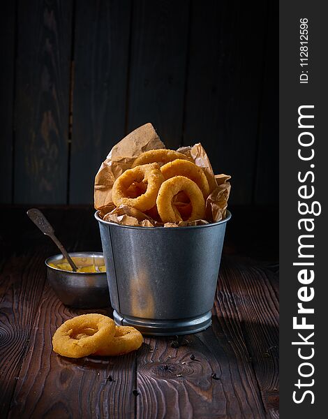 Fried onion rings with sauce served in metal backet on wooden table