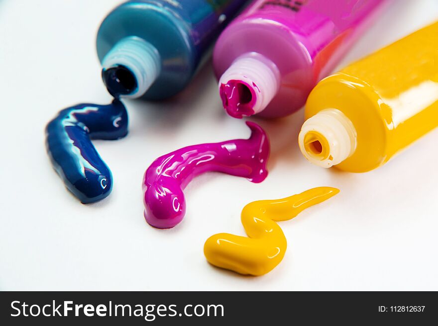 Tubes with acrylic blue, yellow and pink paint on white background