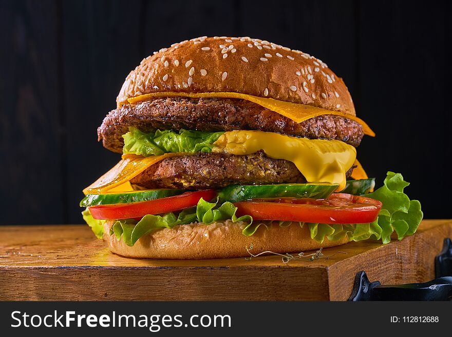 Closeup of home made beef burger with lettuce and tomatoes served on wooden cutting board. Dark background