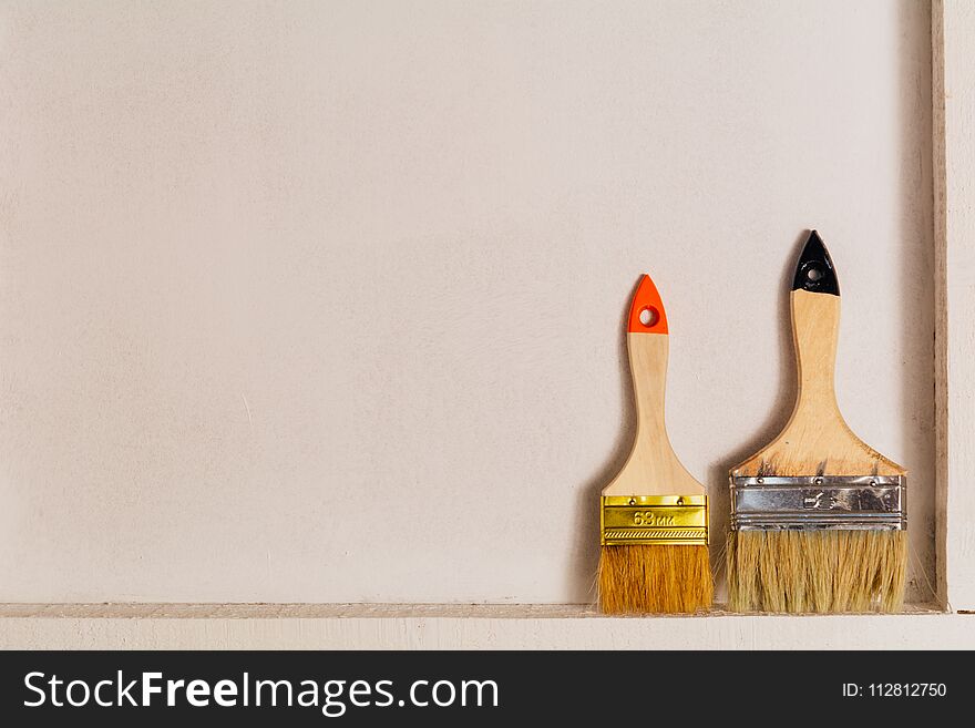 Two paint brushes are exactly on the bars and leaning against a white wall. Two paint brushes are exactly on the bars and leaning against a white wall