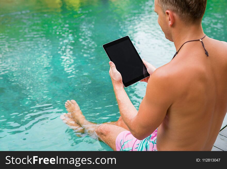 Man using tablet while sitting by the exotic pool. Man using tablet while sitting by the exotic pool