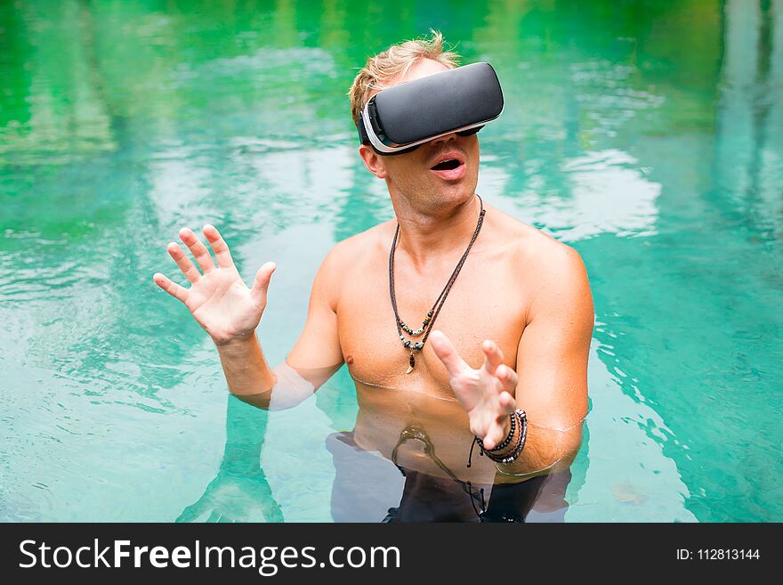 Man in water with virtual reality glasses, man standing in tropical pool with virtual reality glasses