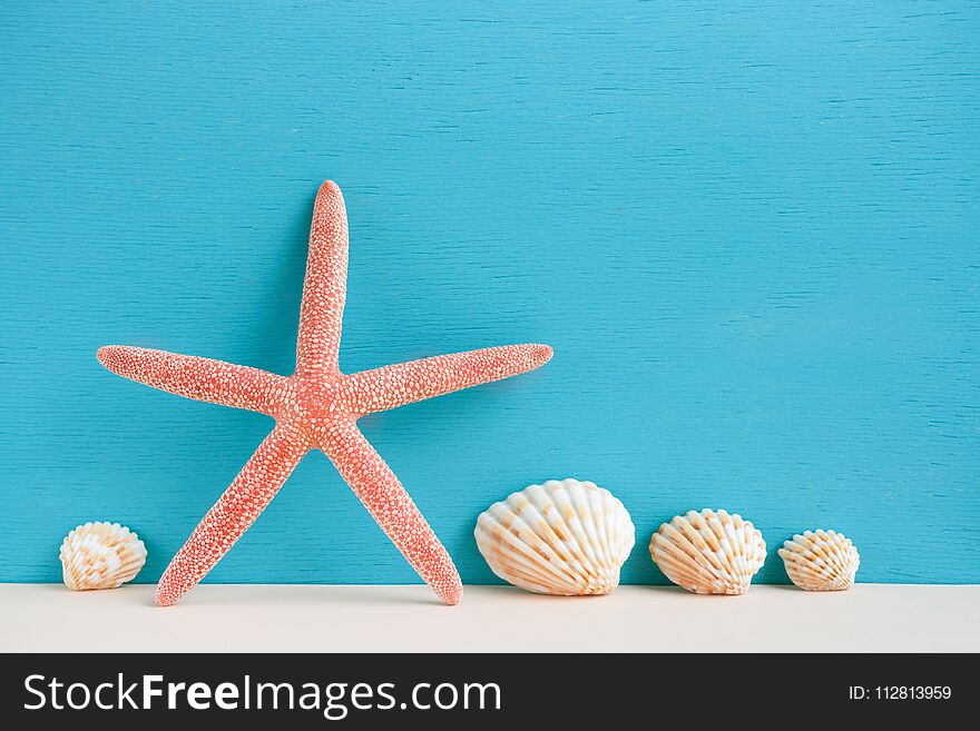 Red starfish and seashells standing on beige surface on turquoise background.