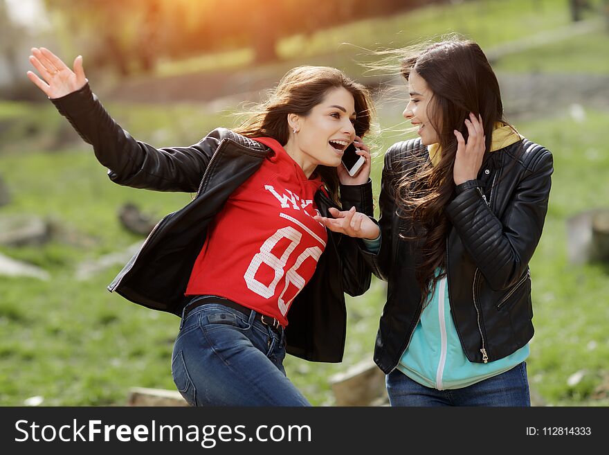 Two pretty and happy young woman using the mobile phone in the park. Best friends.