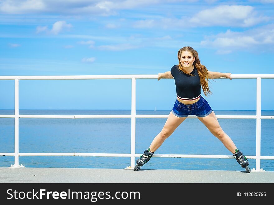 Attractive young woman wearing roller skates relaxing after ride. Fit female having fun during summer time on sea coast. Attractive young woman wearing roller skates relaxing after ride. Fit female having fun during summer time on sea coast.