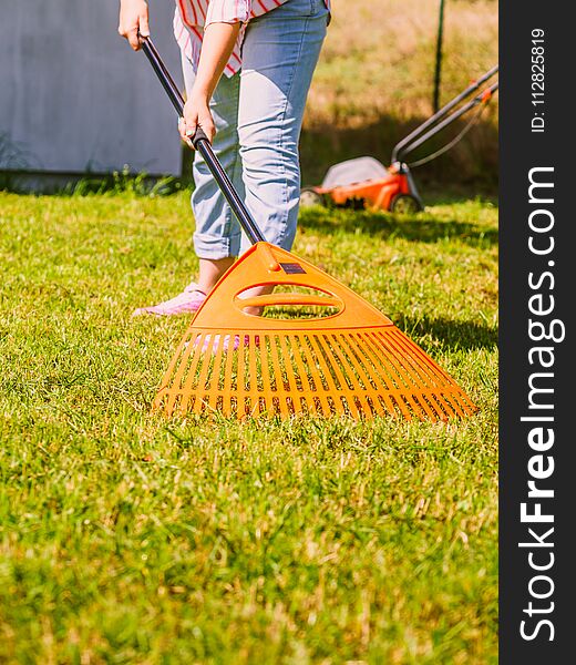 Gardening. Female adult raking green lawn grass with rake tool on her backyard. Gardening. Female adult raking green lawn grass with rake tool on her backyard