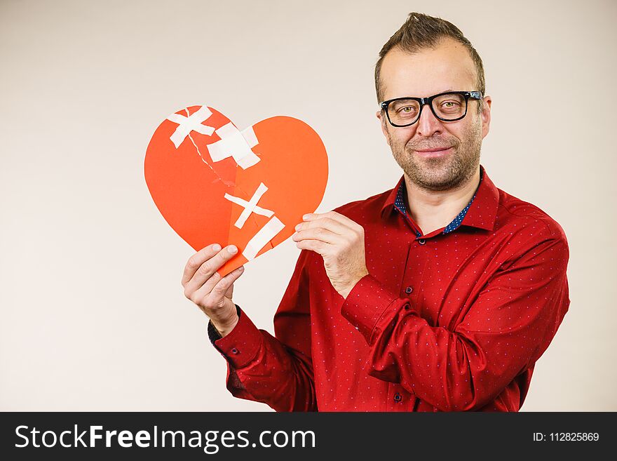 Healed love. Valentines Day concept. Adult smiling man holding big red heart with plaster. Male healing relationship. Healed love. Valentines Day concept. Adult smiling man holding big red heart with plaster. Male healing relationship.