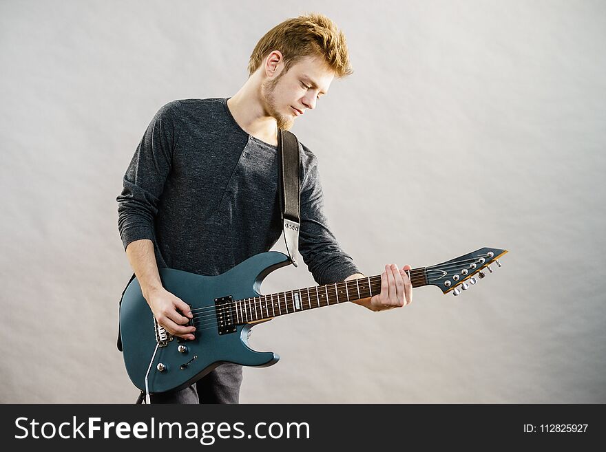 Young bearded man with electric guitar. Adult person is holding instrument and playing. Hobby, music concept, on grey. Young bearded man with electric guitar. Adult person is holding instrument and playing. Hobby, music concept, on grey