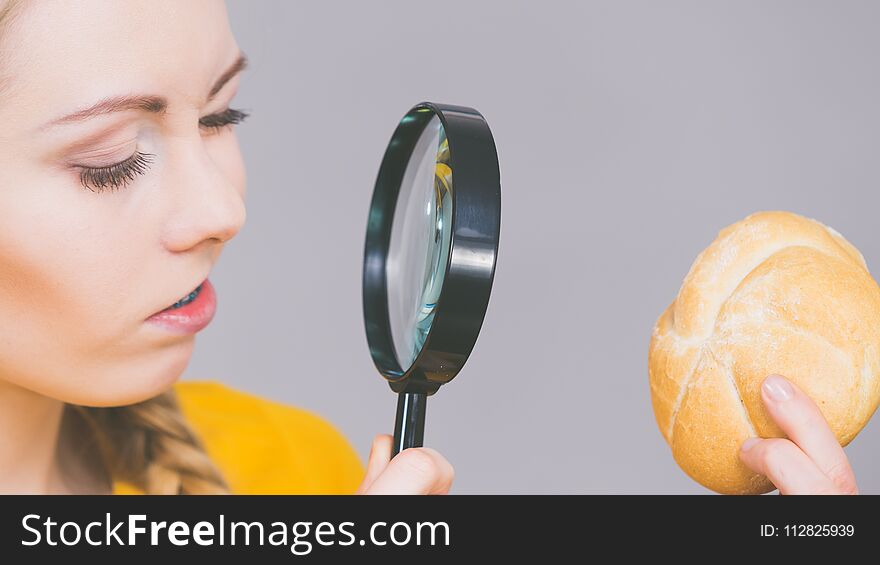 Woman holding bun bread roll and magnifying glass examine wheat product ingredients