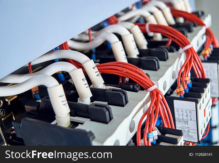 A number of magnetic starters and connected electrical wires in the electrical Cabinet. Cables with tips and digital marking. Red wires are assembled into a bundle of plastic ties. A number of magnetic starters and connected electrical wires in the electrical Cabinet. Cables with tips and digital marking. Red wires are assembled into a bundle of plastic ties.