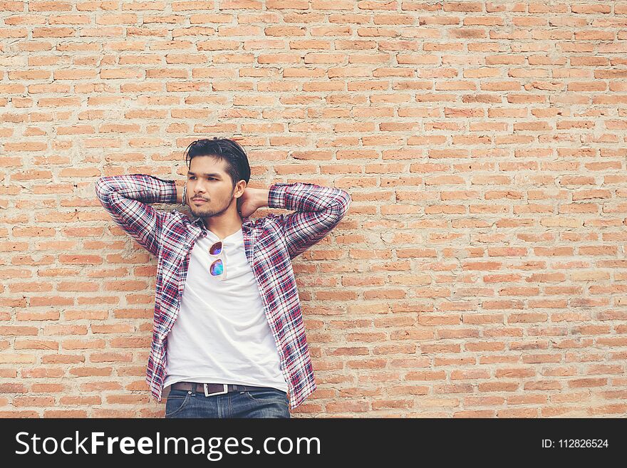 Young handsome hipster man wearing plaid shirt and jeans against a brick wall.