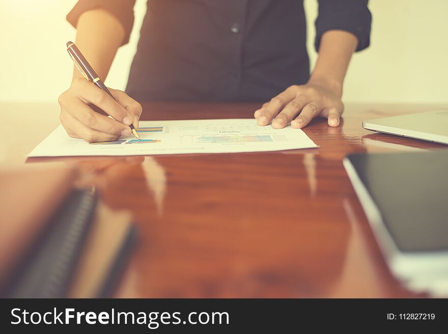 Woman`s hand with a pen writing on the business paper. Report chart,busy at work.