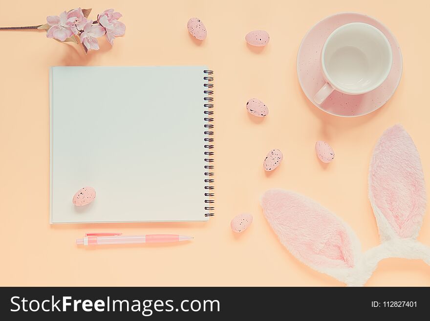 Easter holiday background with notebook and pen, cup for coffee, bunny ears and easter eggs. Copy space background. Flat lay. Toned