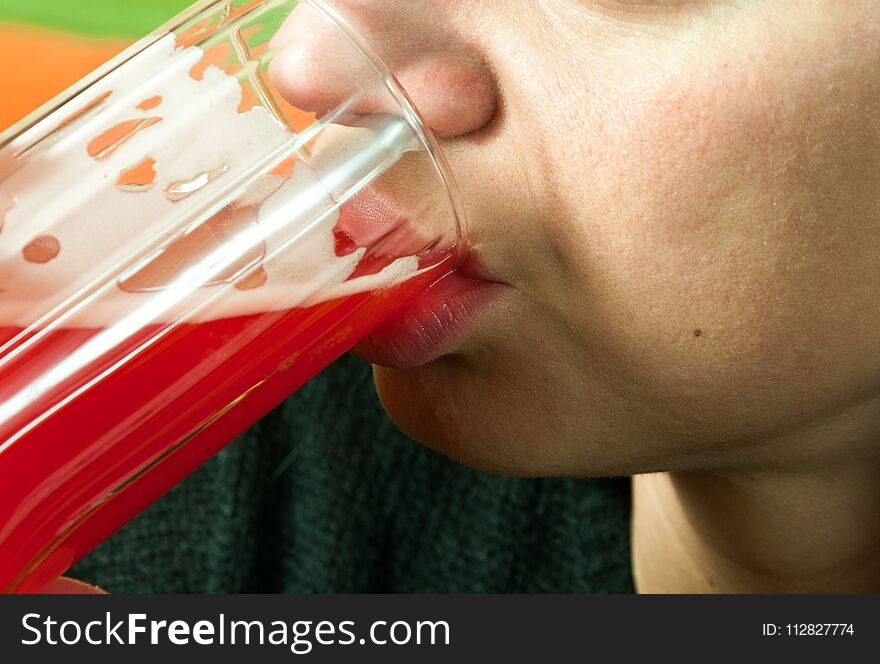 Close up of girls face and lips drinking strawberry red juice from the glass as refreshment, real people, selective focus