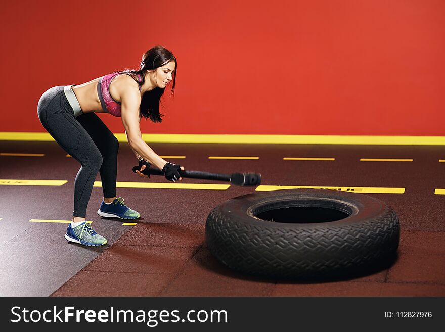 Fit young woman workout in the gym with hammer and tractor wheel.