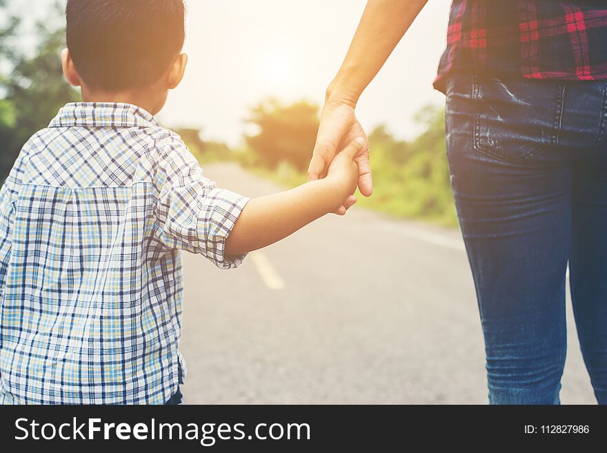 Mother holding a hand of his son in summer day walking on the street.