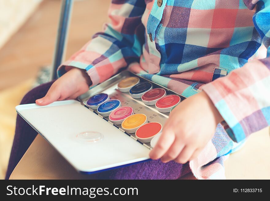 Little cute girl holds a set of color paints for painting face.