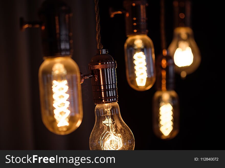 Lamp incandescent spiral retro vintage warm tube edison. Yellow light, dark background, hanging on the ceiling, quirky shape of the spiral. Lamp incandescent spiral retro vintage warm tube edison. Yellow light, dark background, hanging on the ceiling, quirky shape of the spiral.