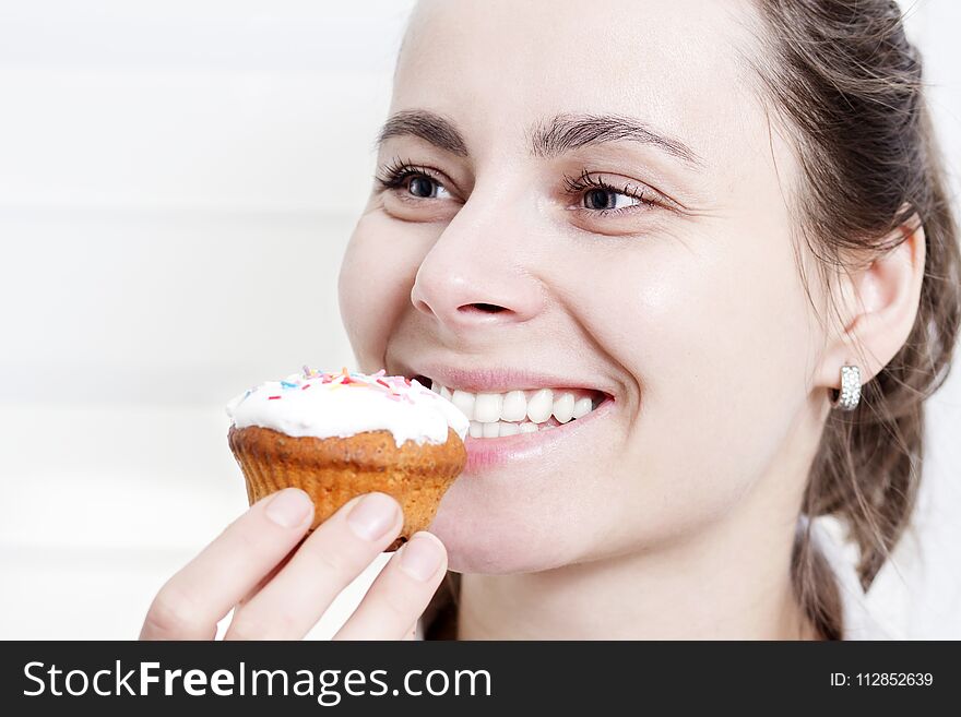 Portrait of smiling girl eating muffin cupcake. Beautiful young attractive caucasian girl face biting muffin