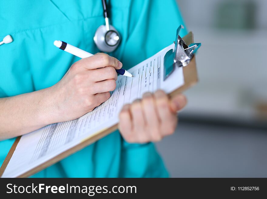 Female doctor filling up medical form on clipboard closeup. Physician finish up examining his patient in hospital and ready to give a prescription to help. Healthcare, insurance and medicine concept.