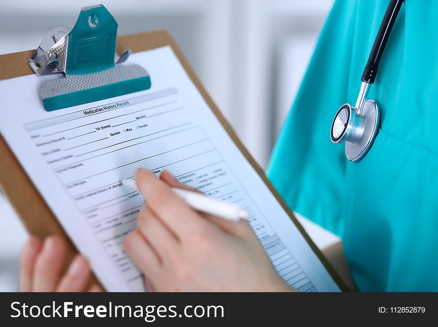 Female doctor filling up medical form on clipboard closeup. Physician finish up examining his patient in hospital and ready to give a prescription to help. Healthcare, insurance and medicine concept.