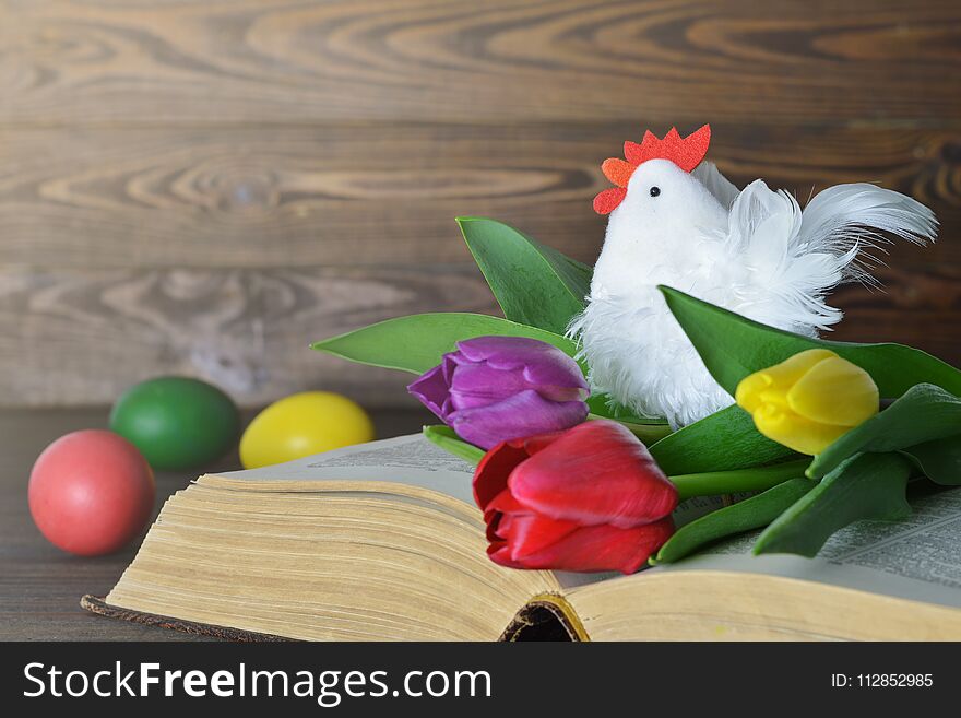 Easter card with colored Easter eggs, rooster toy and tulips on the book