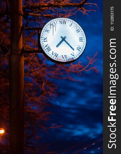 A clock with a glowing dial on a street lamppost at dusk