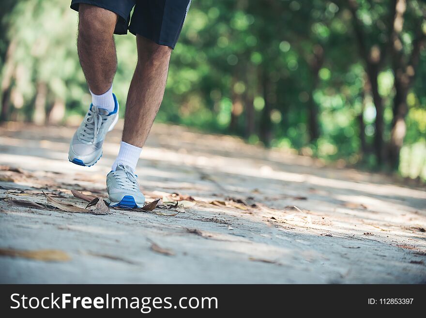 Close up foot of young runner man running along road in the park.