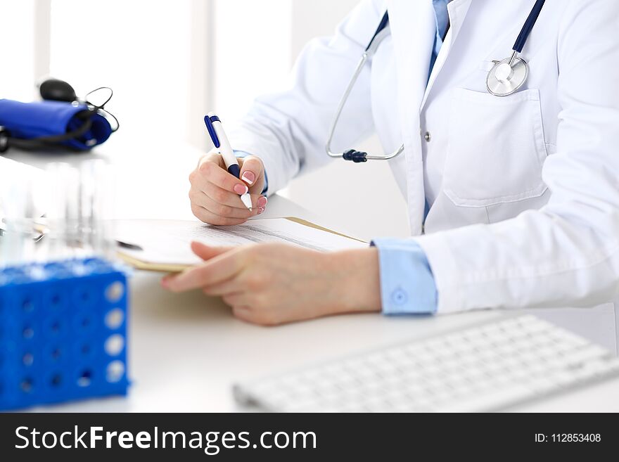 Female doctor filling up medical form on clipboard closeup. Physician finishing up examining his patient in hospital an